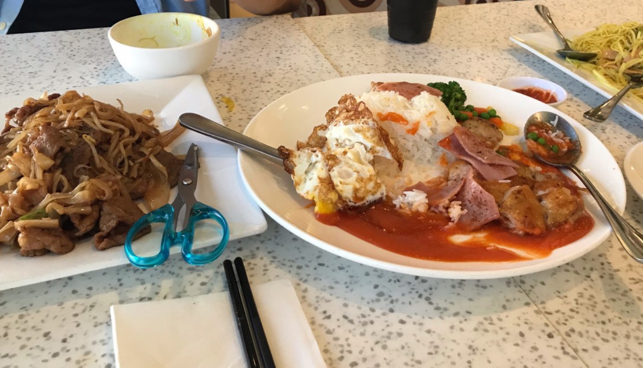 table with three dishes on it. stir fried beef noodles, rice and chicken cutlet with tomato sauce and veggies, and singapore fried vermacelli.